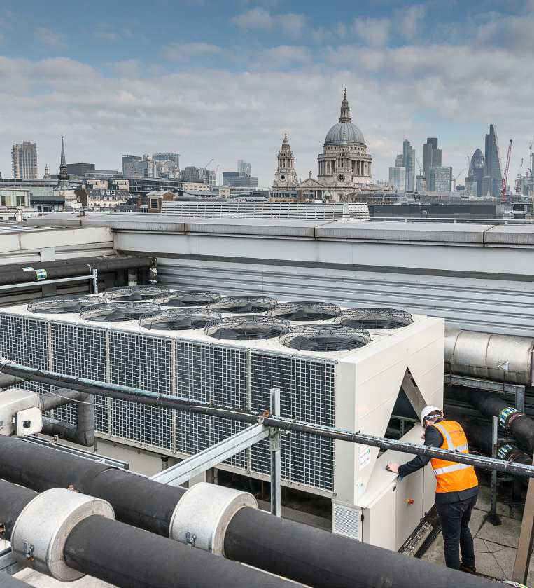 Blu-Red engineer working on a rooftop chiller installation with St Paul's Cathedral and the City of London skyline in the background